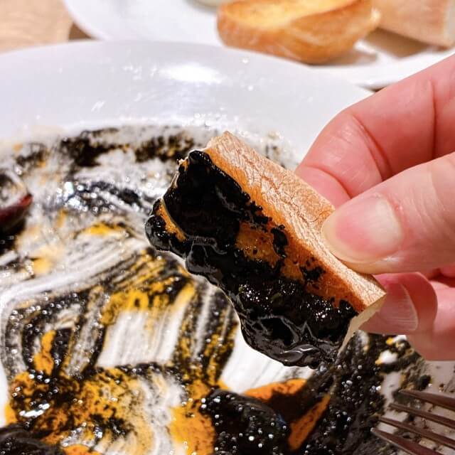 皿に残ったイカ墨ソースをパンで拭っている様子