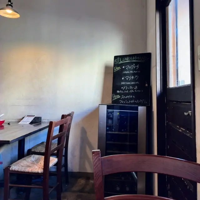 ピッツェリアの店内で、木製の椅子と黒板のランチメニューが並ぶ落ち着いた空間