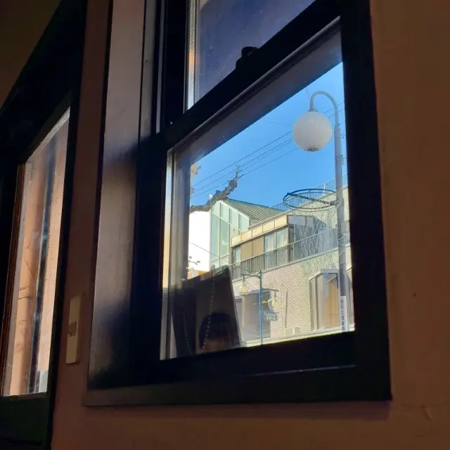 店内の窓越しに、青空と住宅街、白い街灯が見える風景
