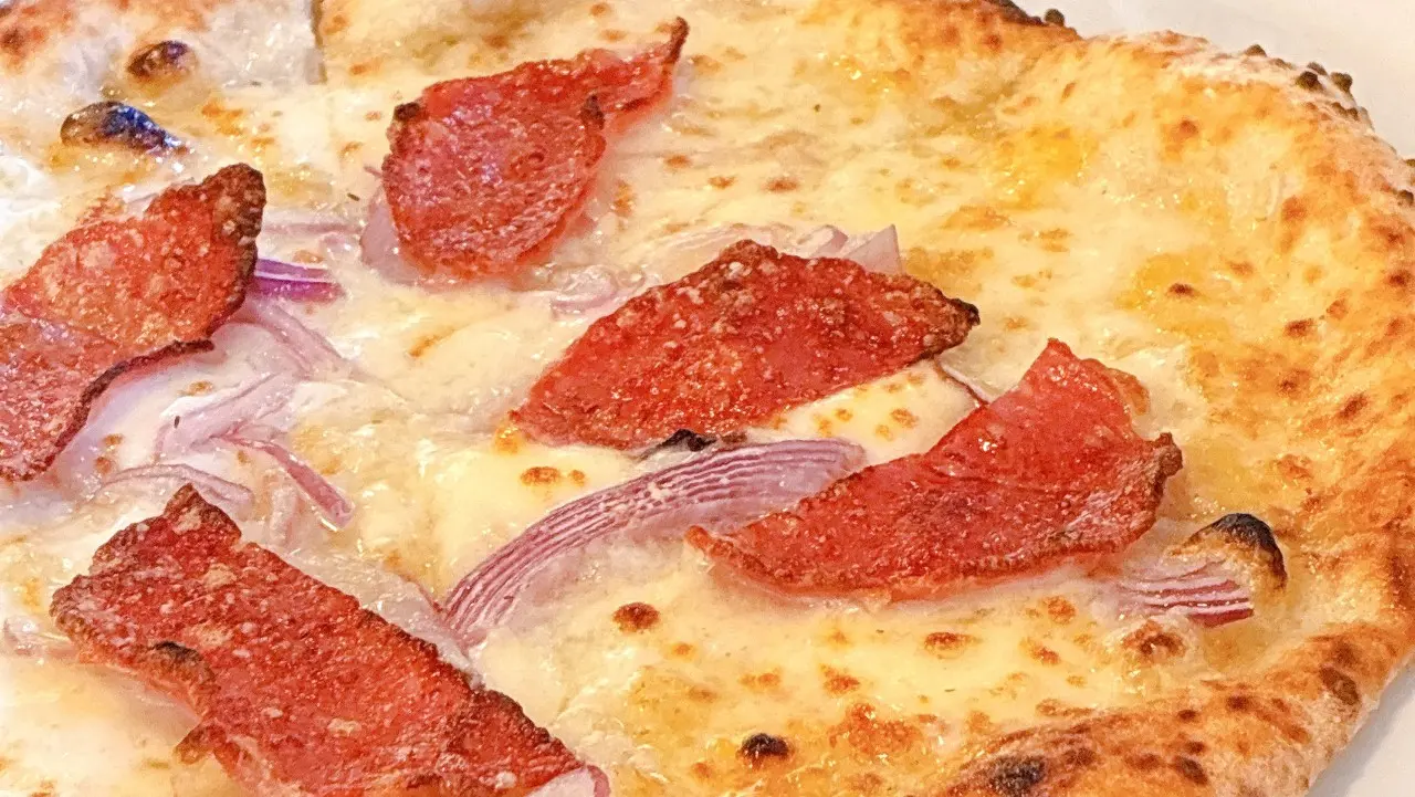 サラミと赤玉ねぎがトッピングされた、香ばしく焼き上がったピッツァ