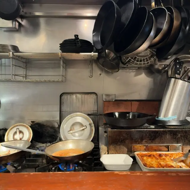 厨房のコンロで調理中のフライパンと、壁に吊るされた多数のスキレット